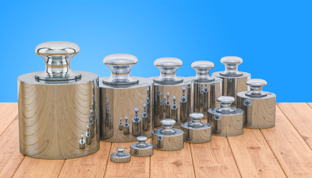 A set of shiny silver calibration weights sitting atop a wooden plank floor in front of a bright blue background